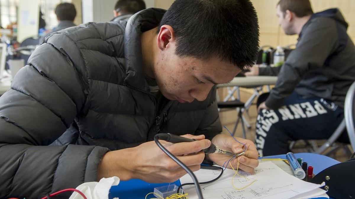 Penn State senior Andy Luo, of State College, solders wires for his group’s wristband during HackPSU on Sunday at the Business Building on Penn State’s campus.