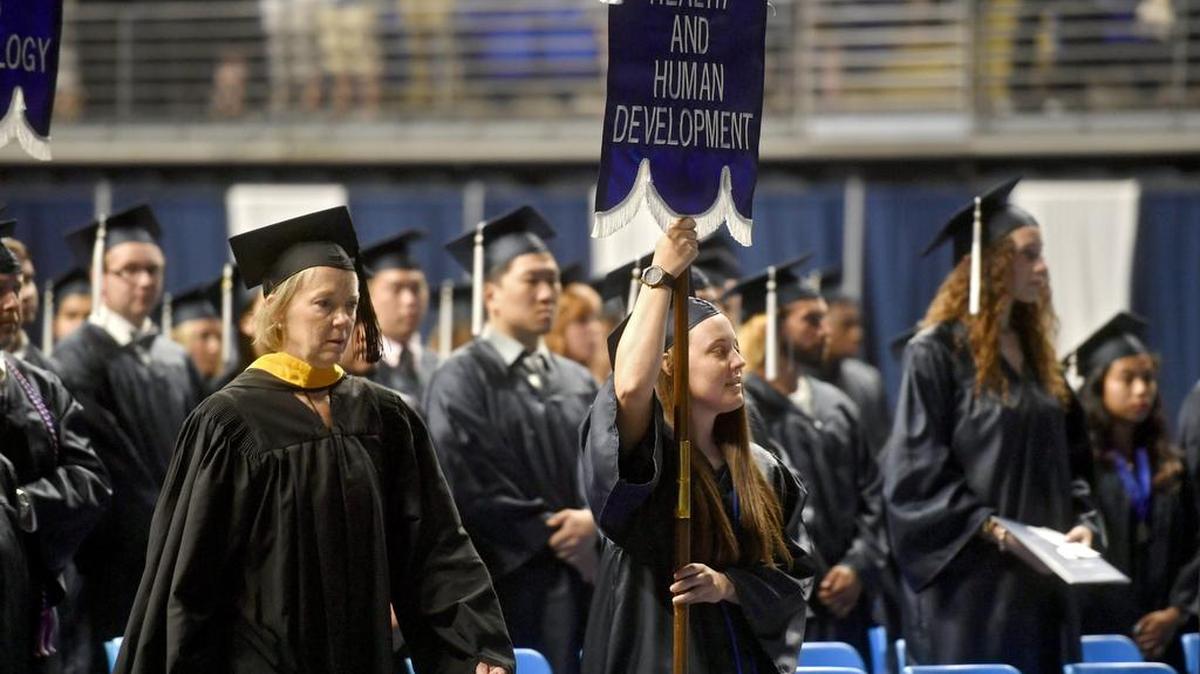 Bellefonte Area High School alum Kashia Quay, accompanied by instructor Patty Kleban, left, carries the banner for college of Health and Human Development as the college’s marshal for Penn State summer commencement on Saturday at the Bryce Jordan Center.