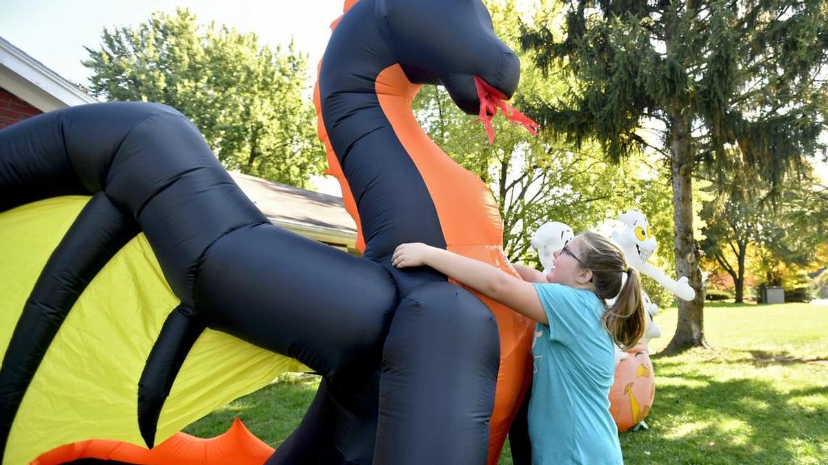 Tayla Jenkins, 9, hugs the inflatable dragon in her family’s front yard on West College Avenue. Over the weekend, all four of their Halloween inflatables were slashed. After being disappointed, the family decided to patch them and continue to decorate with holiday spirit.