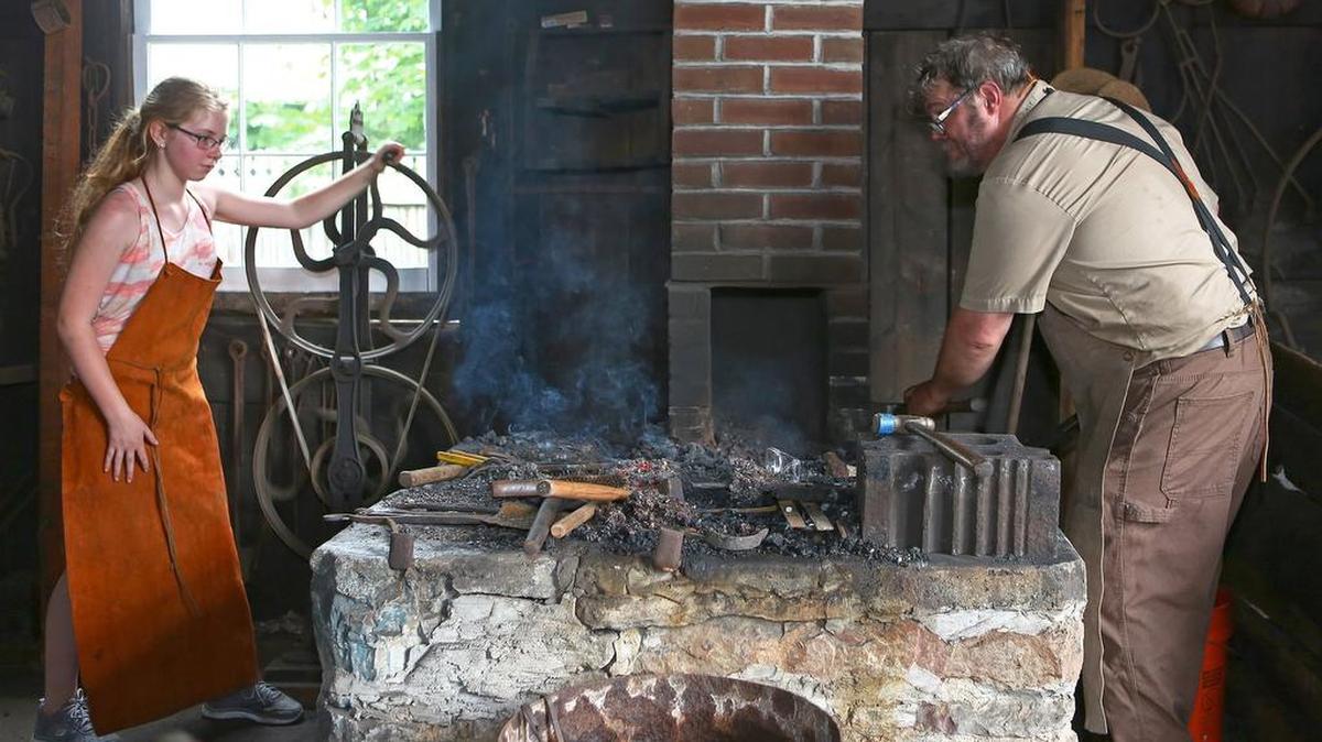 Mount Nittany Middle School student Maeve Flanagan stokes the furnace as Eric Johnson heats the wrought-iron ladel in the Boalsburg blacksmith shop during the 2016 Boalsburg Memorial Day festival.