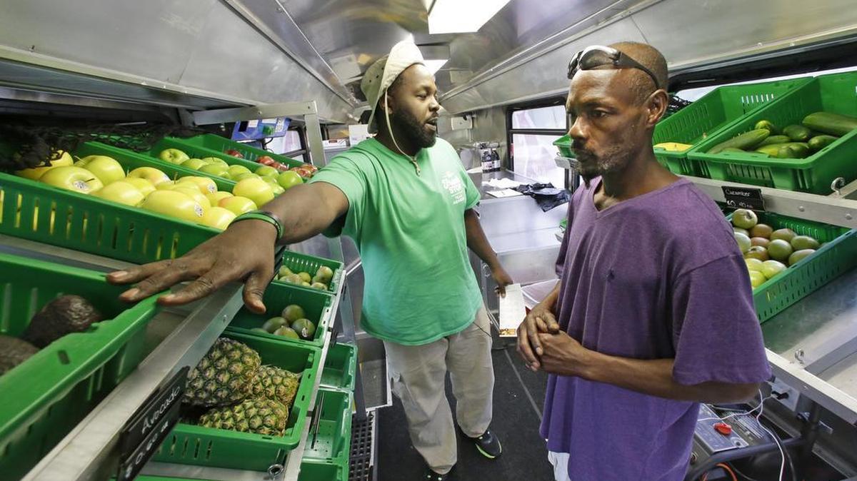 In this Wednesday, July 15, 2015, photo, Fresh Stop employee Jamar Allen, left, helps Jock Riggins as he shops on the Fresh Stop bus, a mobile market, in Eatonville, Fla. The Fresh Stop brings fresh fruits and vegetables to communities with no supermarkets. The nation’s largest grocery chains have built new supermarkets in only a fraction of the neighborhoods where they’re needed most, according to an analysis of federal food stamp data by The Associated Press.