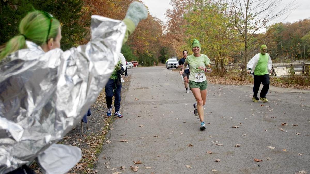 “Queen T” Teresa Timmerman is cheered into the transition zone by her teammates, decked out in green and waving an avocado, during the 15th Annual Tussey Mountainback 50 Mile Relay and Ultramarathon on Sunday, October 18, 2014.