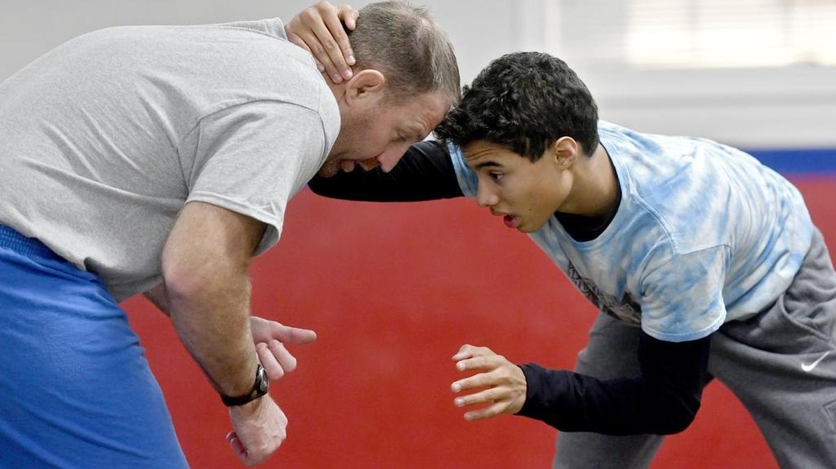 St. Joseph’s Catholic Academy wrestling coach Pat Flynn, left, explains a move to Julian Simmons and the team during practice on December 20. Flynn is trying to build a tradition for the young Wolves.