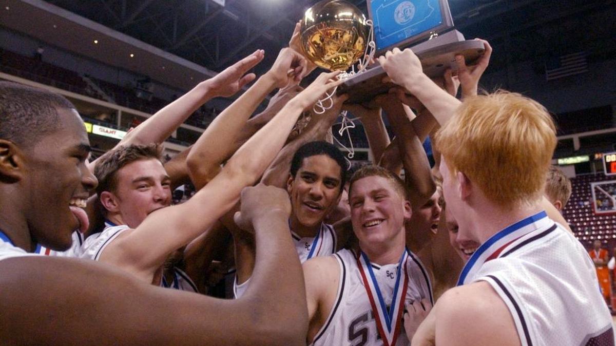 State College players raise the state title trophy after defeating Chester in overtime at the PIAA Class AAAA Boys’ Basketball Championship in Hershey on March 22, 2003.