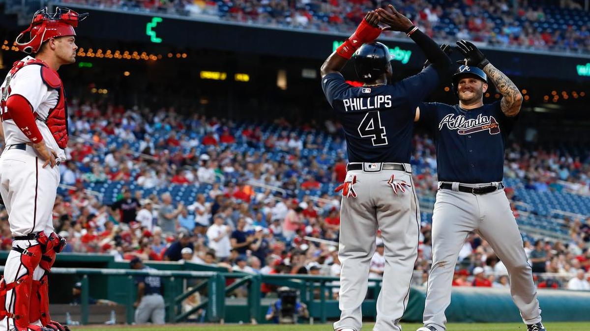 As Washington Nationals catcher Matt Wieters (32) looks on at left, Atlanta Braves first baseman Matt Adams (18) celebrates with teammate Brandon Phillips (4) as he crosses the plate after hitting a three run homer in the third inning of a baseball game at Nationals Park, Monday, June 12, 2017, in Washington.