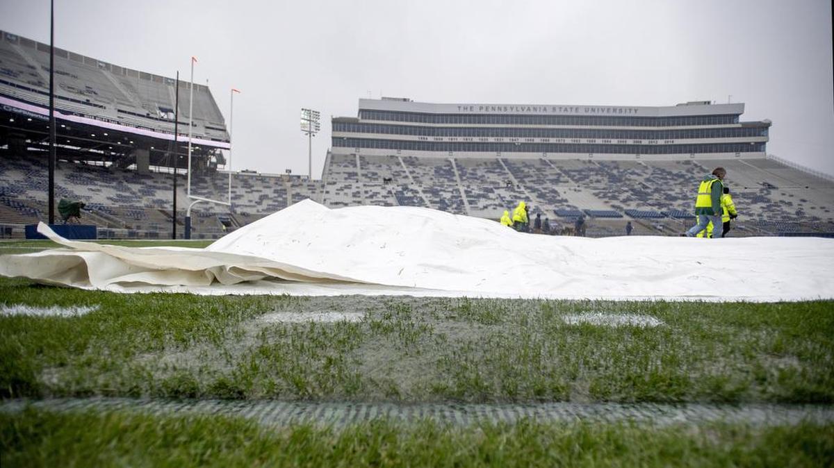 Water pours out off the tarps as the grounds crew pulls them off the field at Beaver Stadium for the Penn State game against Iowa on Saturday, Oct. 27, 2018.